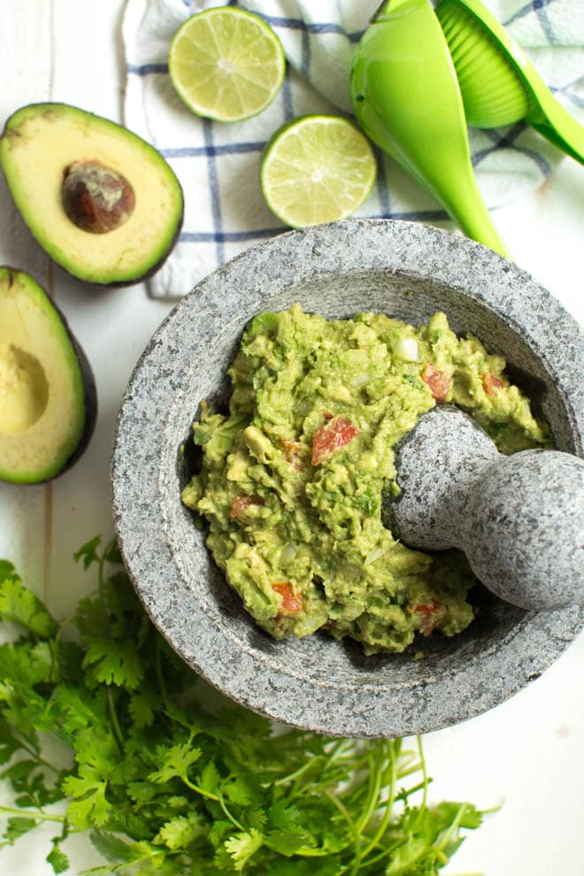 guacamole in a mortar with a pest and avocado plus limes on the side