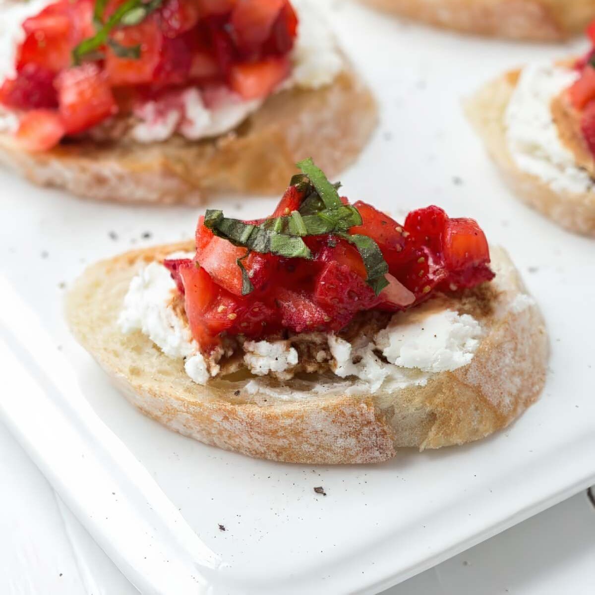 Close-up of strawberry bruschetta with goat cheese, fresh basil, and balsamic on toasted baguette slices