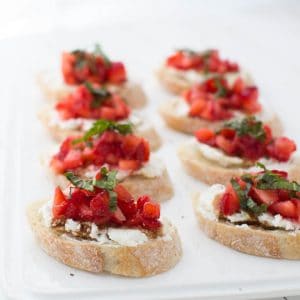 eight slices of strawberry bruschetta sitting on a white plate on a white table