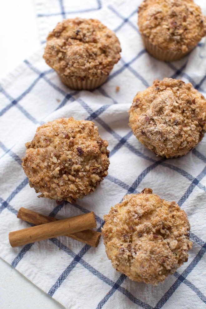 five coffee cake muffins sitting on a check blue kitchen towel with a cinnamon stick garnish on the side