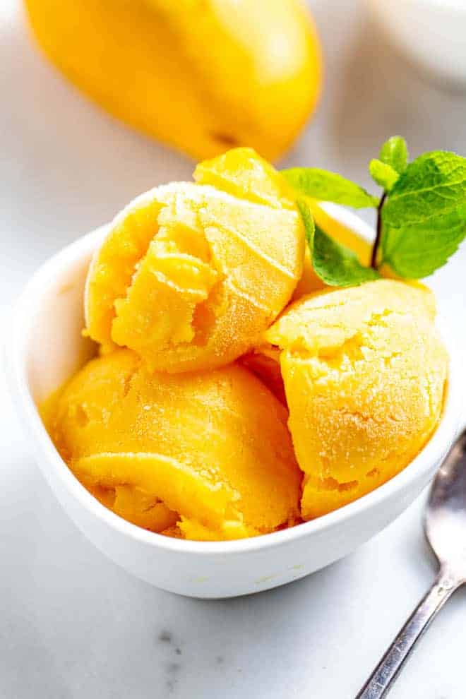 Three scoops of mango sorbet in a white bowl.