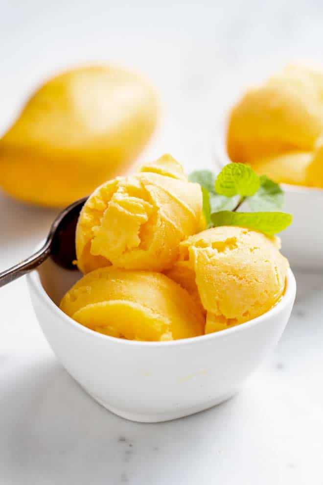 Three scoops of mango sorbet in a white bowl with a spoon.