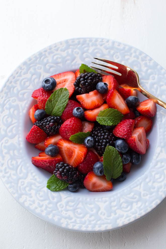 light blue bowl with blueberries, blackberries and strawberries plus mint on top