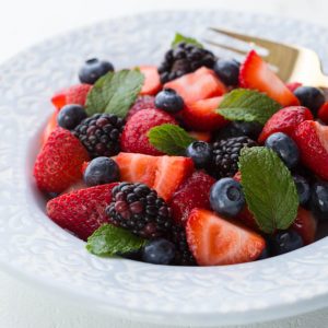 a bowl with strawberries, blueberries and blackberries with mint on top