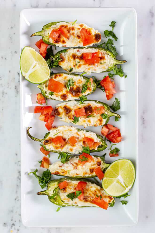 Seven grilled stuffed jalapeno peppers on a plate. 