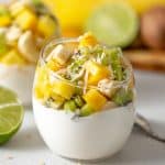clear glass jar filled with greek yogurt with mango, kiwi, banana and pineapple chunks piled on top