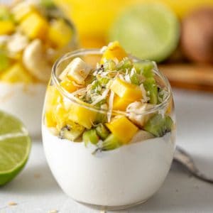 clear glass jar filled with greek yogurt with mango, kiwi, banana and pineapple chunks piled on top