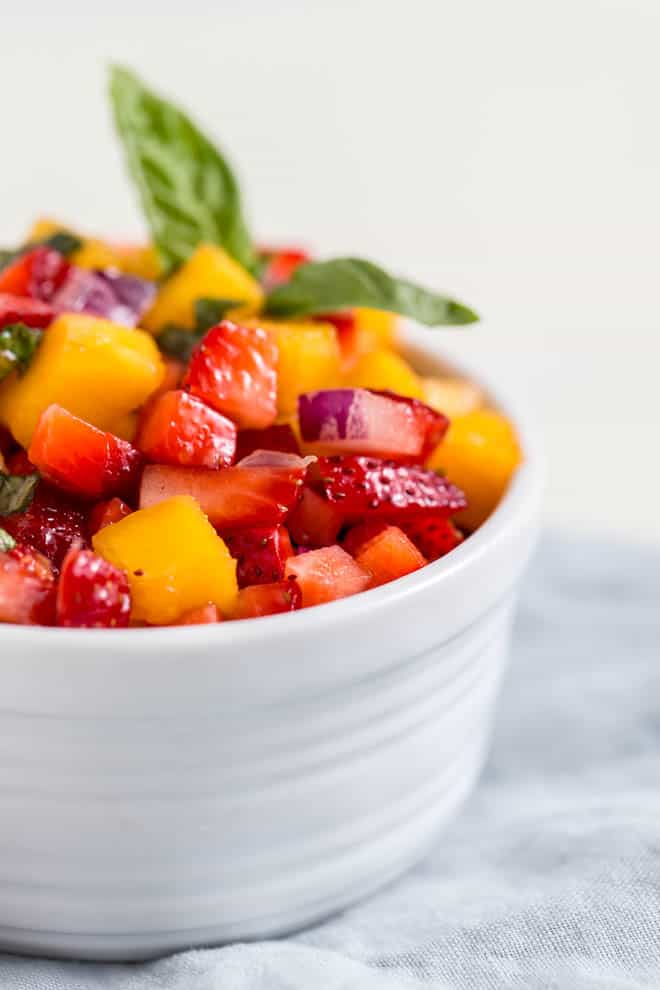 A small bowl of strawberry mango salsa sitting on a light blue napkin.