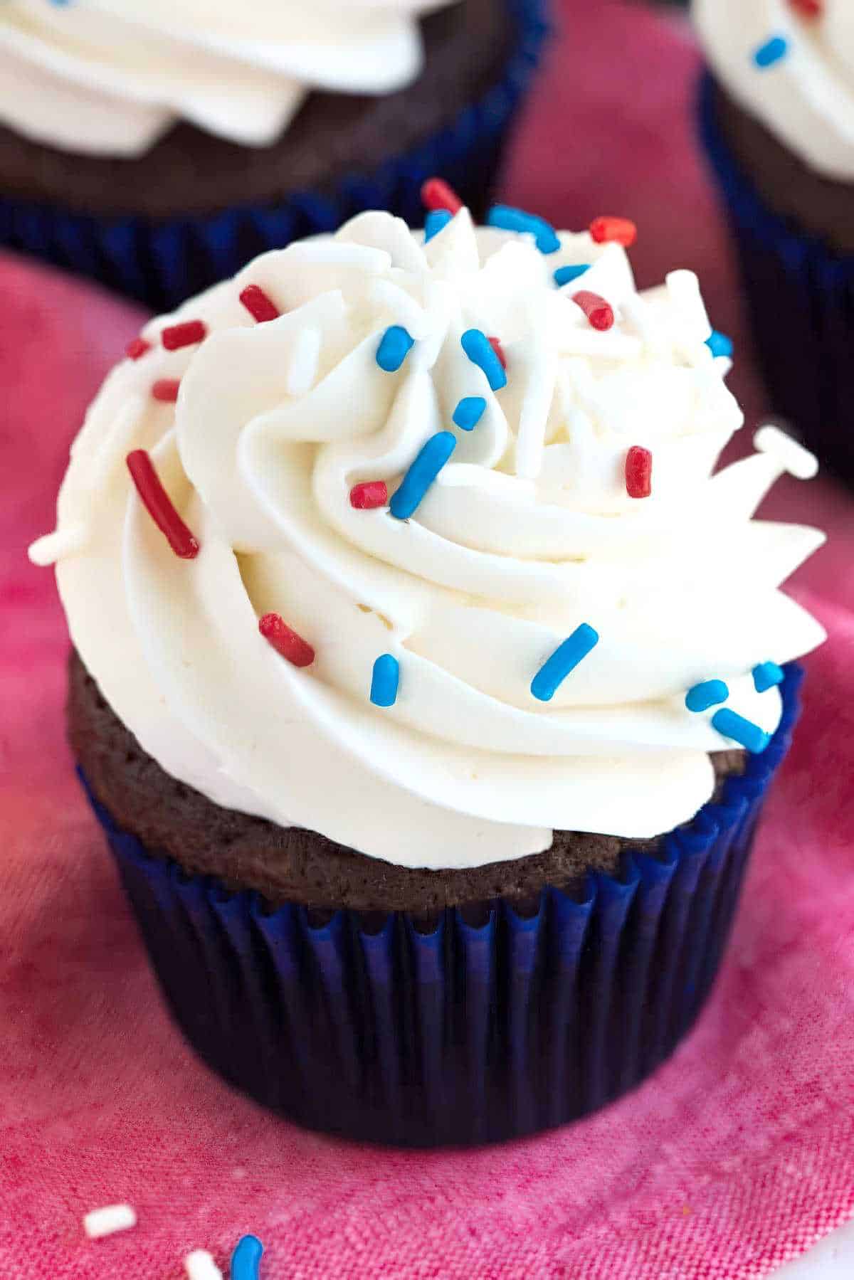 Close-up of a chocolate cupcake with a swirl of vanilla buttercream frosting and sprinkles.