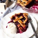 a slice of blueberry pie with a scoop of ice cream on a white plate with a fork