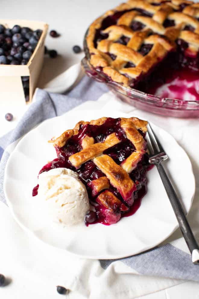 a slice of blueberry pie with a scoop of ice cream on a white plate with a fork