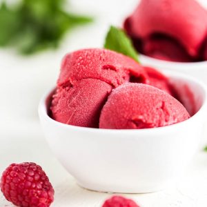 Two scoops of raspberry mint sorbet in a white bowl on a white table.