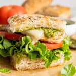 bread stacked with lettuce, tomato, grilled chicken, mozzarella cheese and pesto to create a sandwich.