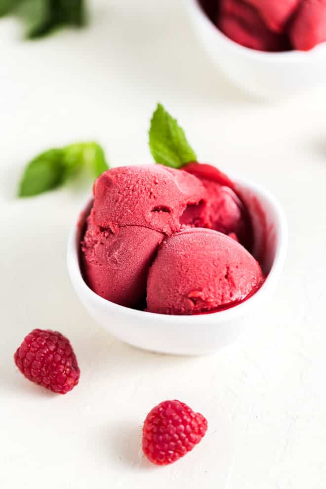 Three scoops of raspberry sorbet in a white bowl on a white table