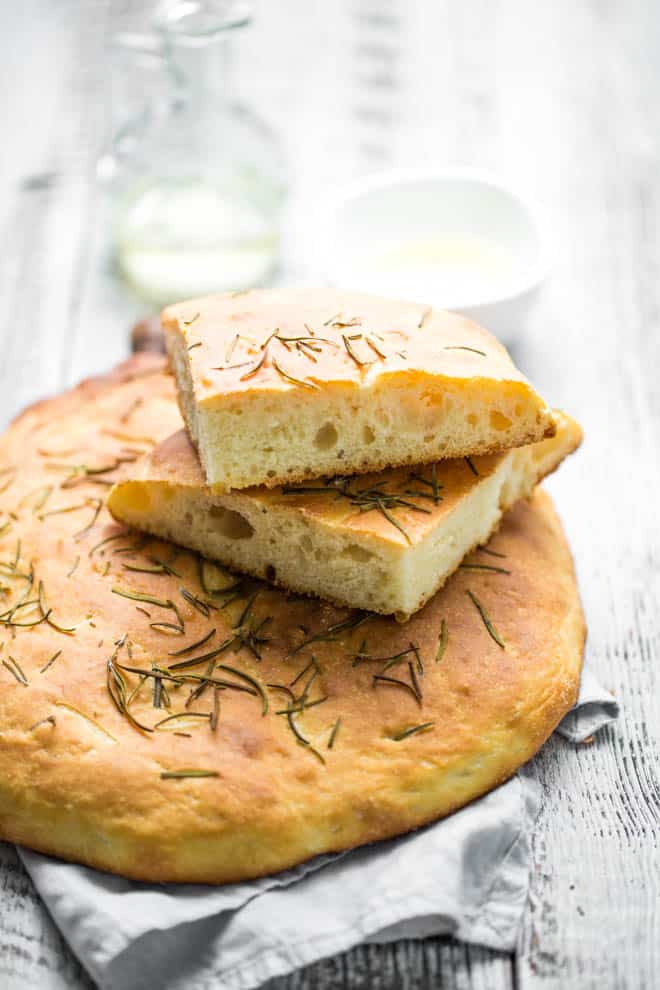 A loaf of rosemary focaccia bread with cut pieces of bread on top.