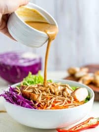 Pouring peanut sauce into a bowl of thai chicken salad.