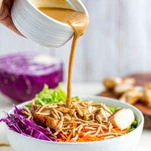 Pouring peanut sauce into a bowl of thai chicken salad.