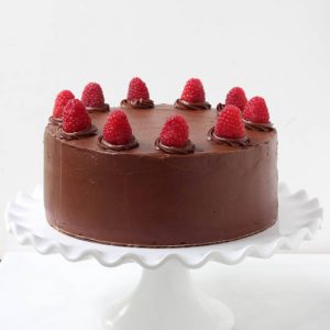 Chocolate Cake with fresh raspberries on top sitting on a white cake platter.