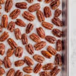 candied pecans on a piece of white parchment paper on a baking sheet