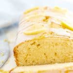 one slice of lemon cake sitting in front of the remaining loaf on a white table
