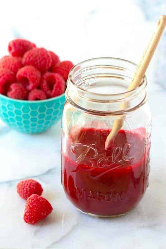 A mason jar with homemade raspberry sauce and fresh raspberries on the counter.
