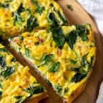 a slice of ham and spinach frittata sitting on a cutting board