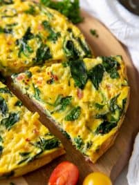 a slice of ham and spinach frittata sitting on a cutting board