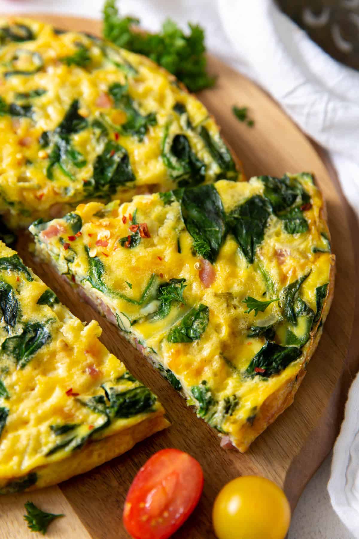 a slice of ham and spinach frittata sitting on a cutting board