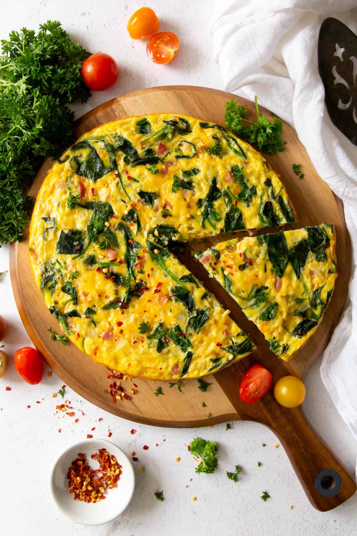 ham and spinach frittata on a cutting board with tomatoes and parsley on the side as garnish