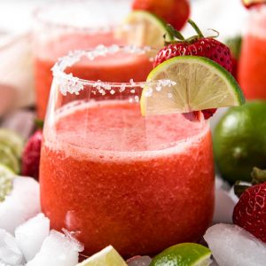 a clear glass with a frozen strawberry margarita in it, garnished with lime and strawberry