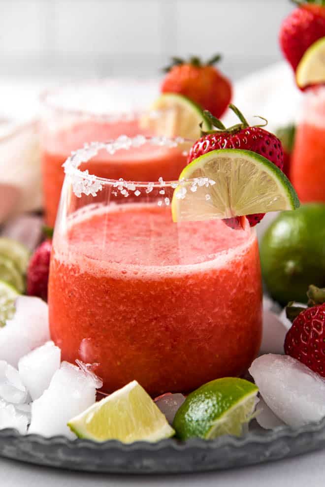 a clear glass with a frozen strawberry margarita in it, garnished with lime and strawberry