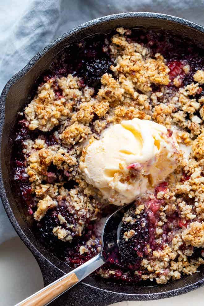 A skillet of warm berry crisp with a scoop of vanilla ice cream.