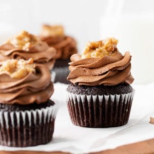 three german chocolate cupcakes sitting on a piece of parchment paper