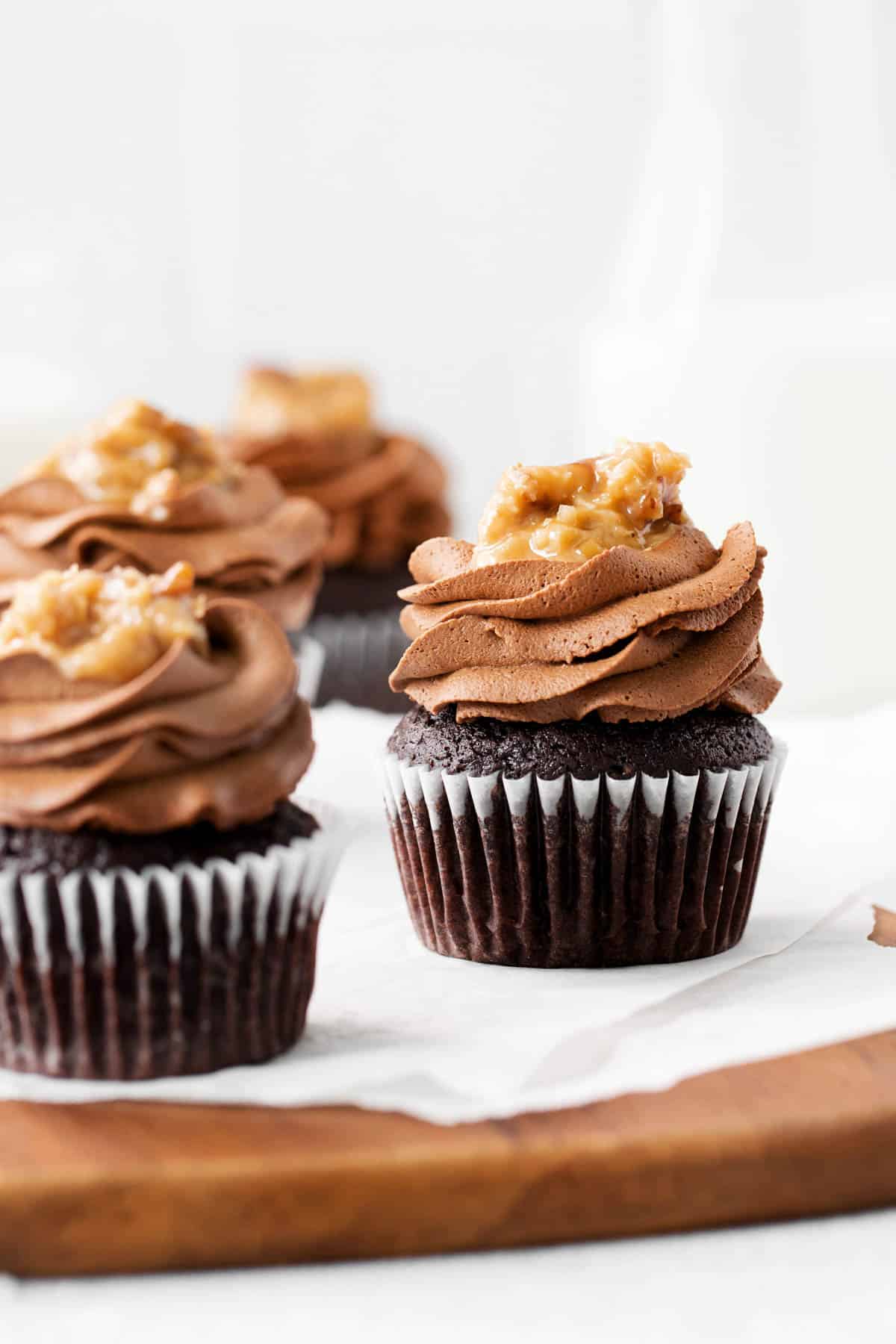 three german chocolate cupcakes sitting on a piece of parchment paper