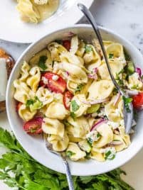 A bowl of tortellini pasta salad with tomatoes, onions and parsley.