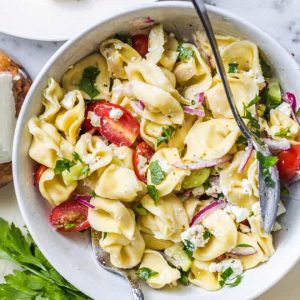 A bowl of tortellini pasta salad with tomatoes, onions and parsley.