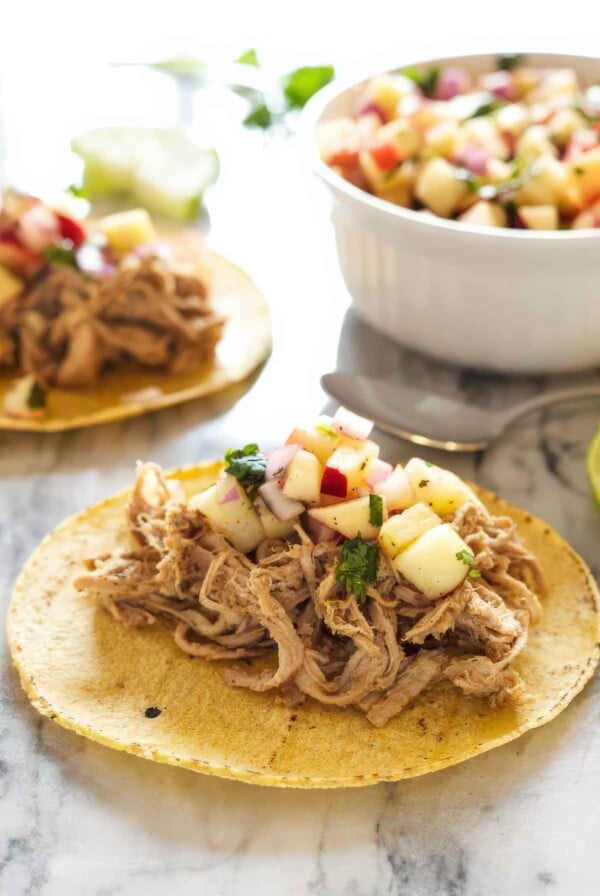 Close-up of a pork carnitas taco topped with crisp apple salsa on a warm corn tortilla.