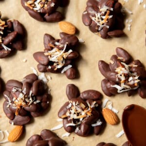 dark chocolate almond clusters on a piece of parchment paper with shredded coconut on top