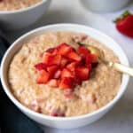 A bowl of strawberry oatmeal with fresh strawberries on top.