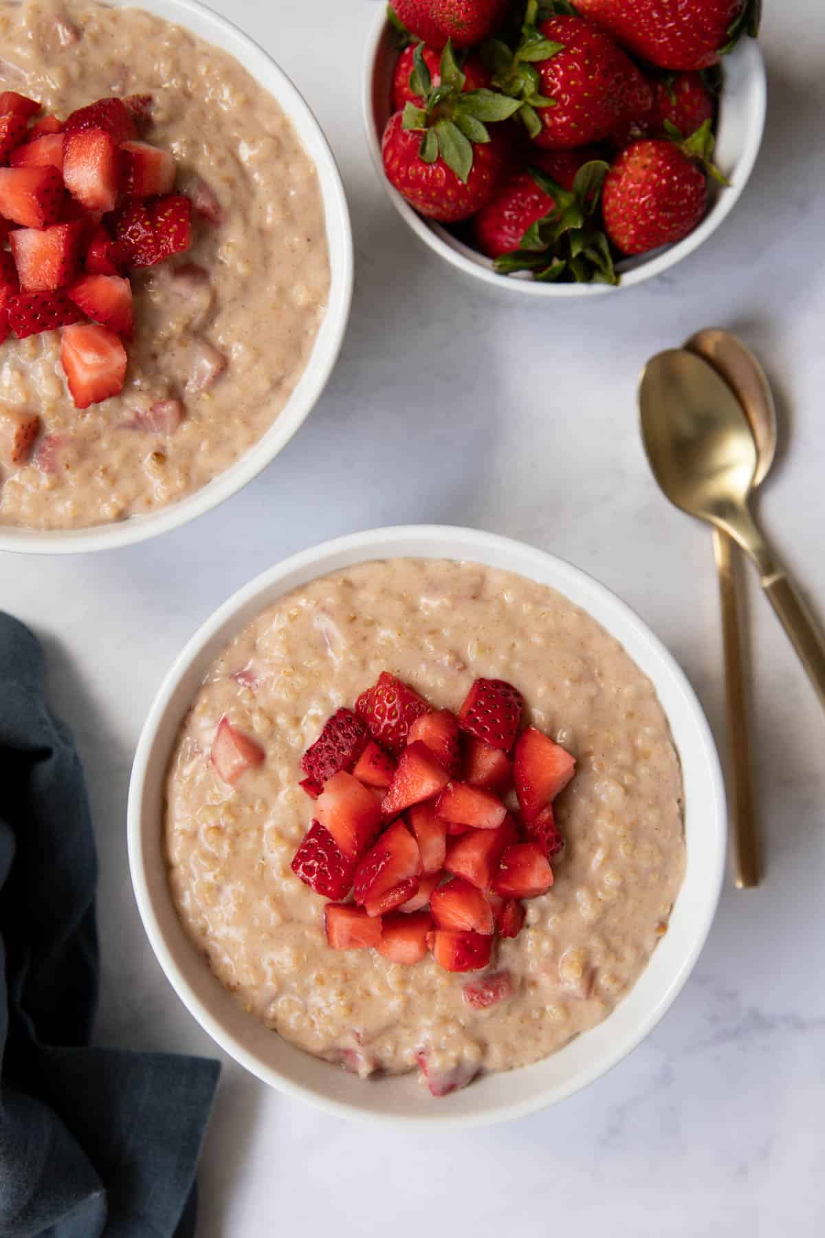 Two bowls of strawberry oatmeal on a tabletop with spoons on the side.