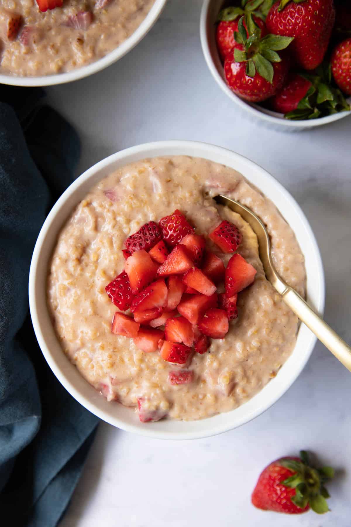 A close up of a bowl of strawberries and cream oatmeal with fresh chopped strawberries on top.