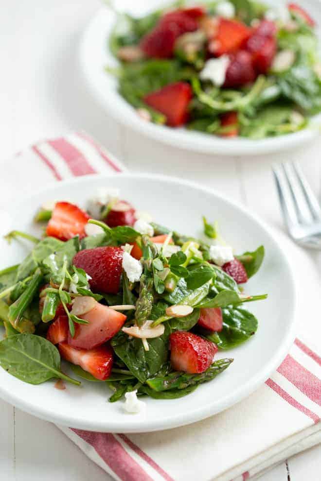 Strawberry spinach asparagus salad on a white plate on a white table.