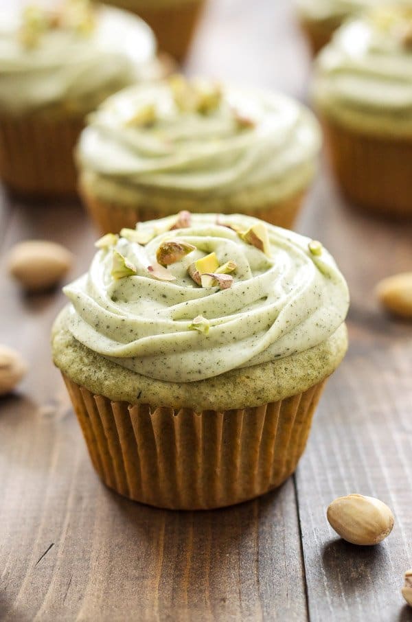 one matcha green tea cupcake sitting on a wooden table in front of other green tea cupcakes