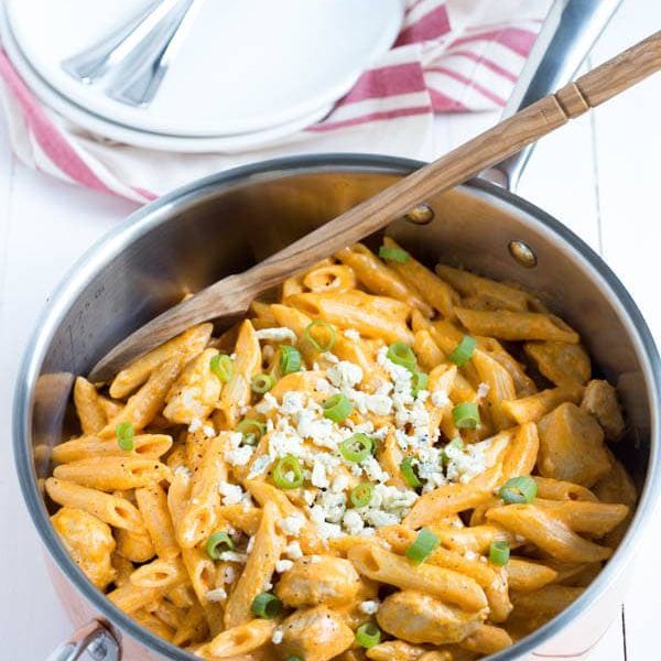 a pan with buffalo chicken pasta sitting on a white table with a spoon in it