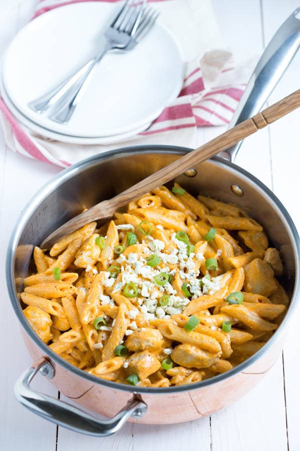 a pan with buffalo chicken pasta sitting on a white table with a spoon in it
