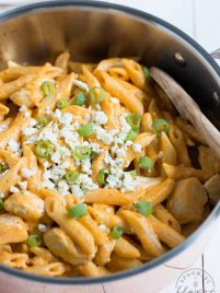 buffalo chicken pasta in a pan with blue cheese crumbles and green onions sprinkled on top