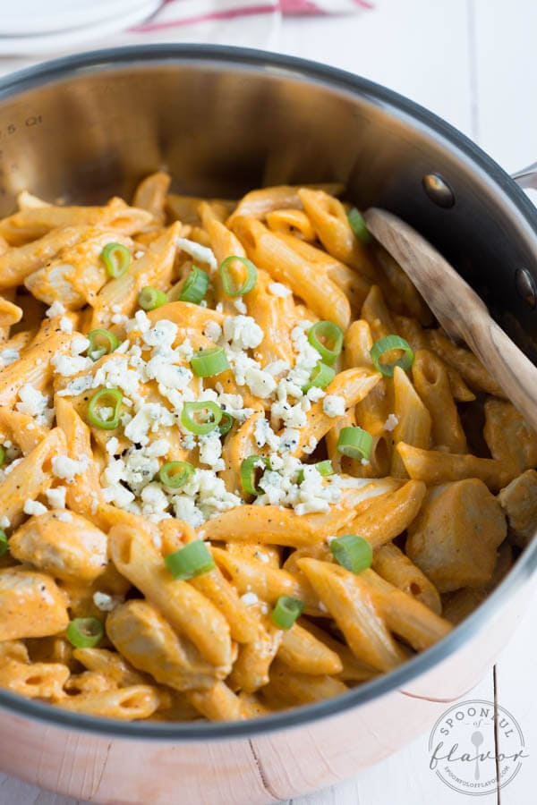 buffalo chicken pasta in a pan with blue cheese crumbles and green onions sprinkled on top