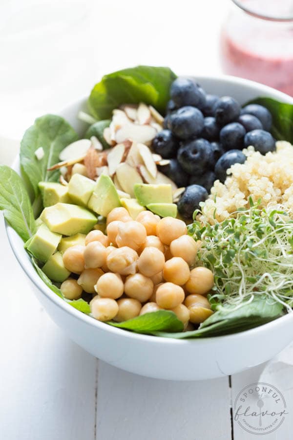 Spring Superfood Bowl with Blueberry-Ginger Dressing - a bed of fresh greens is topped with blueberries, quinoa, sprouts, chickpeas, avocado, almonds and blueberry-ginger dressing!