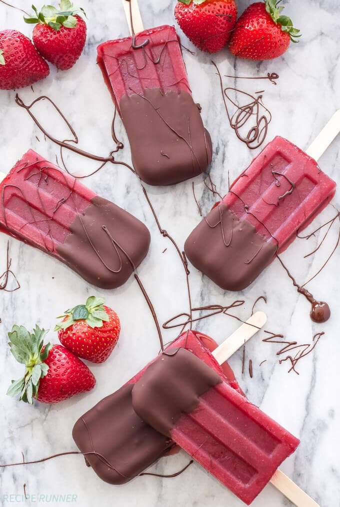 Five popsicles sitting on a white background with strawberries.