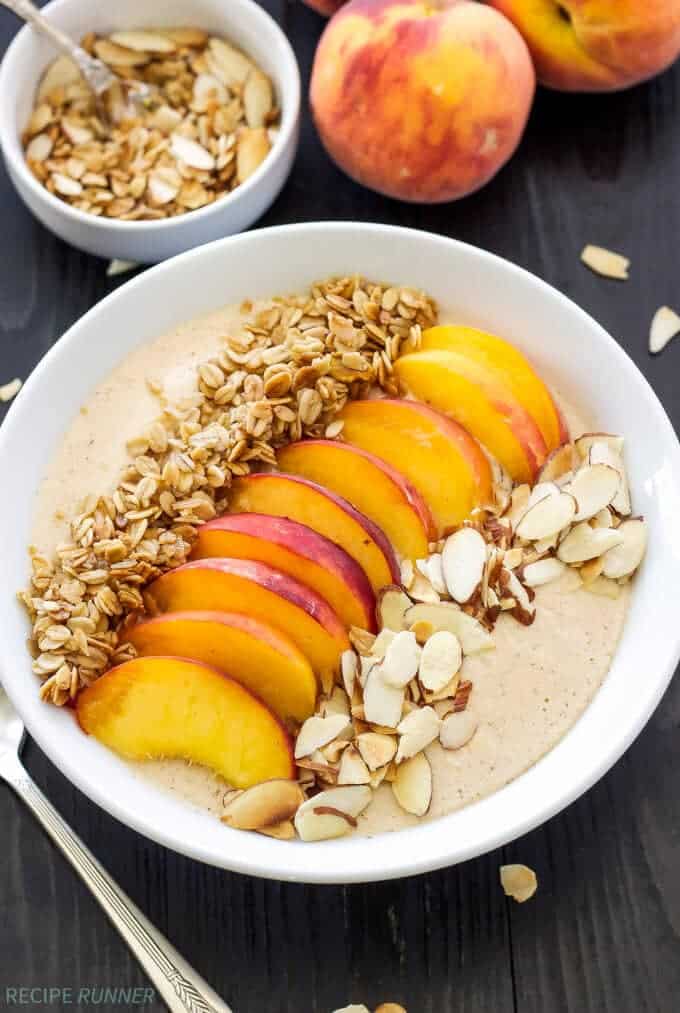 Peach pie smoothie in a white bowl topped with freshly sliced peaches, granola and sliced almonds.